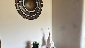 A corner with a wooden console table, a potted plant, a decorative metal wall piece, and a white shelf with a spiral design. - Apartment Obstgarten, 55 sqm, 2 bedrooms, max. 4 persons (Lindau)