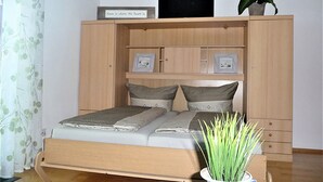 Une chambre à coucher avec un lit, une armoire, une télévision et une plante.