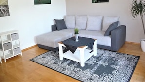 Un salon avec un canapé gris, une petite table blanche, un tapis à motifs et des œuvres d’art murales.