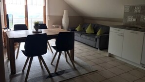 A dining area with a table and chairs, a sofa with cushions, a vase, and a kitchen area with cabinets. - Apartment 'Seeblick' with Shared Garden, Balcony and Wi-Fi (Lindau)