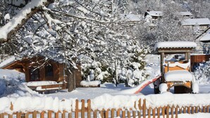 Una cabaña de madera con techo nevado, rodeada de árboles cubiertos de nieve y una valla de madera.