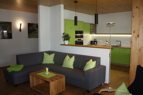 Ein modernes Wohnzimmer mit einem grauen Sofa, grünen Kissen, einem Holztisch und einer Stehlampe.