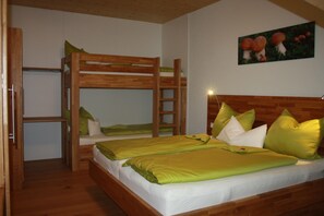 Ein Schlafraum mit Etagenbetten, einer Holzleiter, einer grünen Bettdecke und einem an der Wand hängenden Bild von Pilzen.