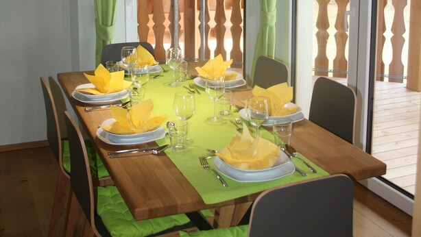 Comedor con mesa de madera dispuesta para seis, cortinas verdes y lámparas colgantes.