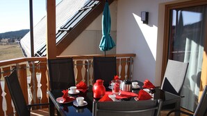 A balcony with a table set for two, chairs, a red umbrella, and a view of the landscape. - Apartment 'Hochtalblick' with Mountain View, Shared Garden and Wi-Fi (Ibach)