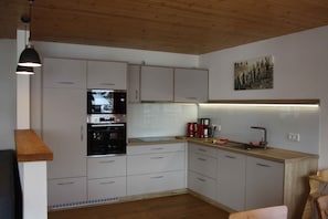 Uma cozinha moderna com armários brancos, forno embutido, cafeteira e bancada de madeira.