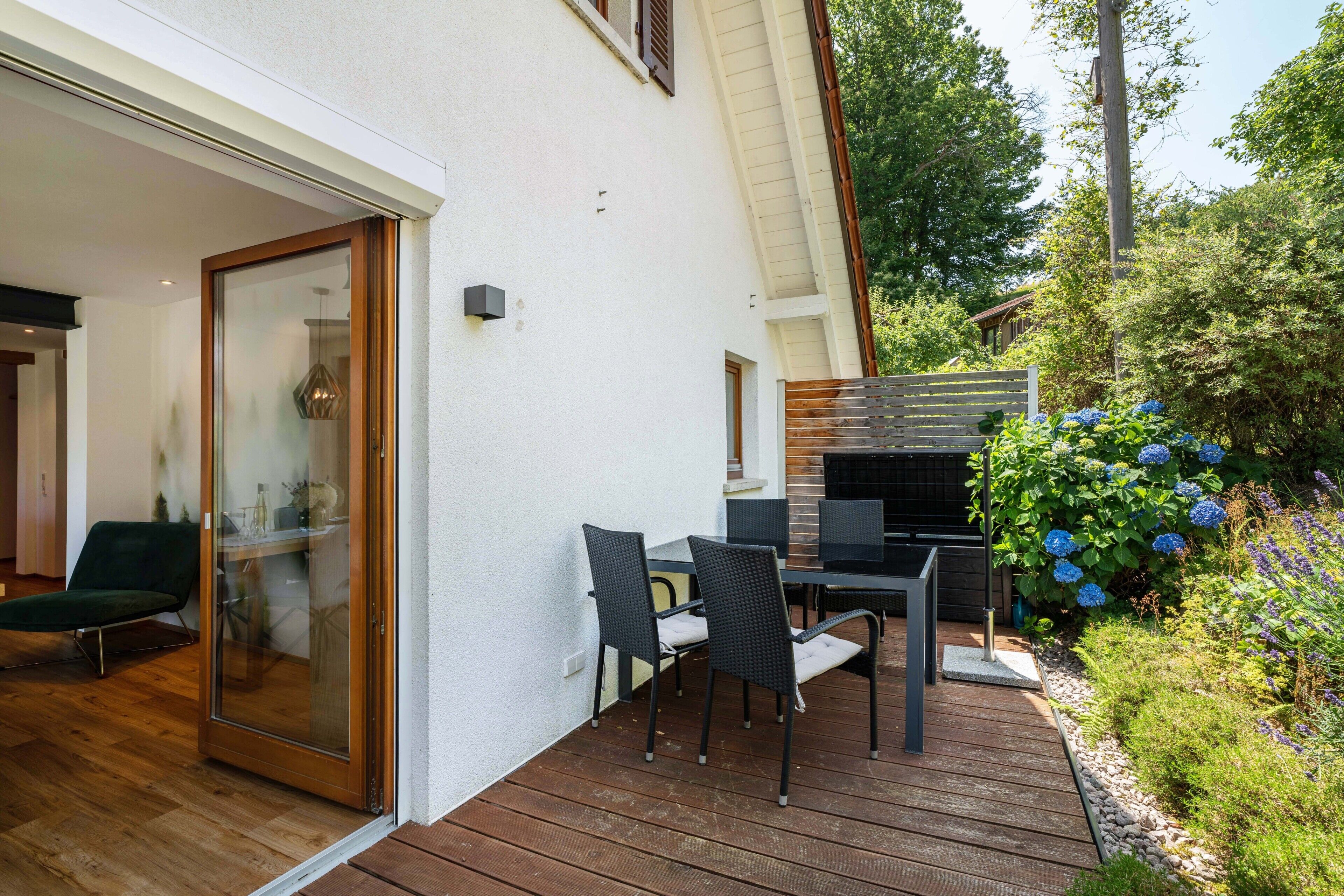 Un patio exterior moderno con una mesa y sillas para comer, un gran ventanal corredizo y una terraza de madera.