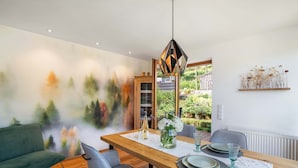 A dining area with a wooden table, grey chairs, a hanging pendant light, and a wall mural.