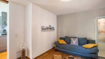 Een moderne woonkamer met een grijze bank, houten vloer en een glazen deur.