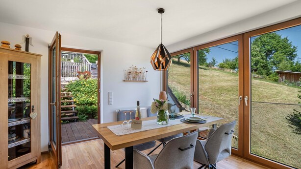 A dining area with a wooden table, chairs, a pendant light, and a view of a garden through large sliding doors.