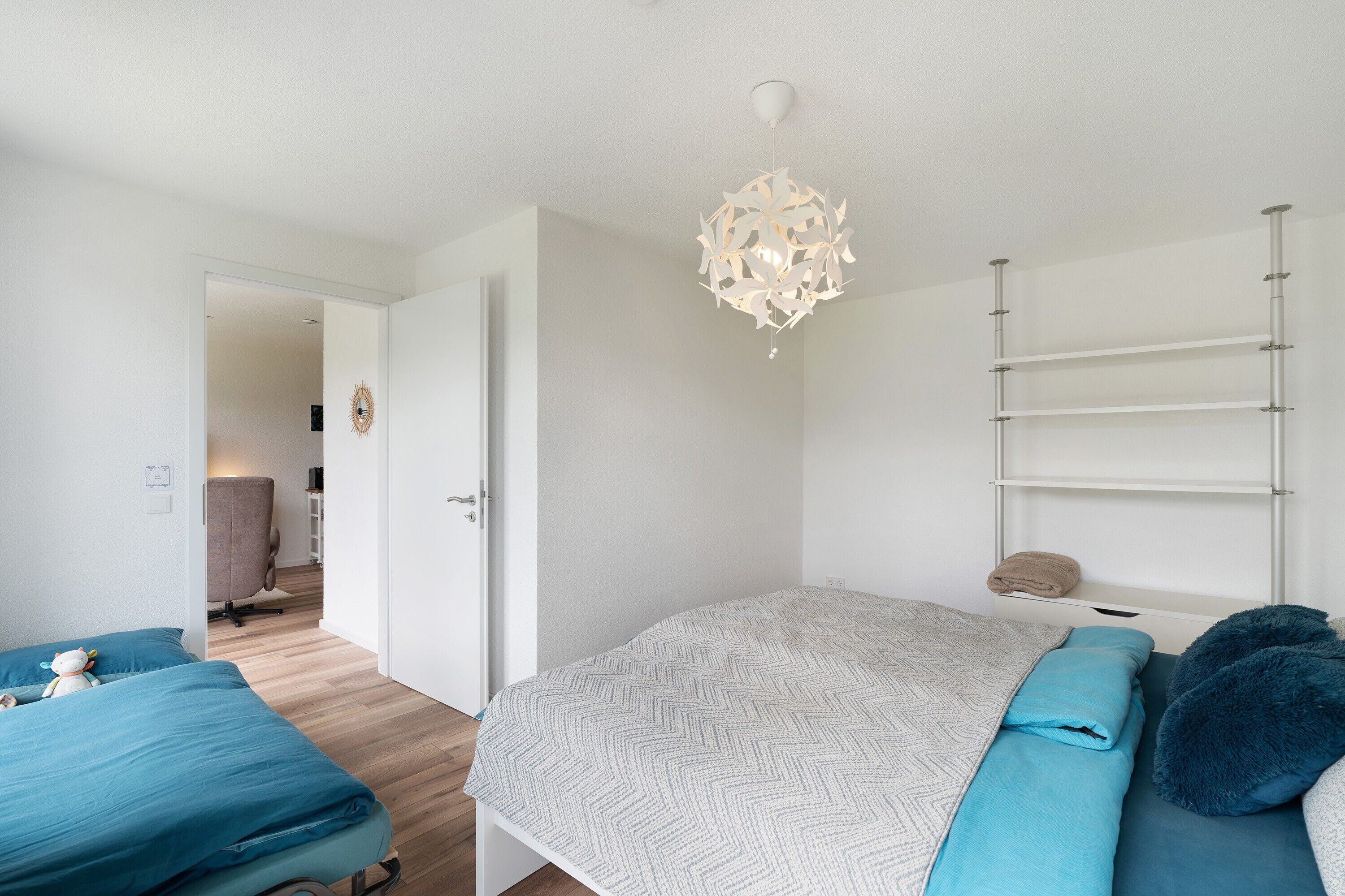 A bedroom with a bed, a desk, a chair, and a hanging light fixture.