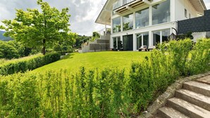 Ein modernes Haus mit großer Glasfassade, einem gepflegten Rasen und einer Steintreppe.