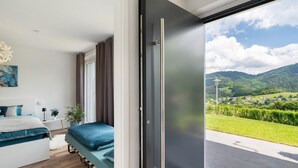 A bedroom with a bed, a potted plant, and a view of a green landscape through a sliding door.