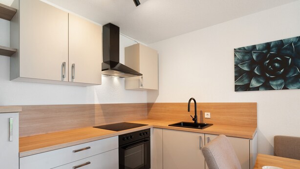 A compact kitchen with a stove, oven, and sink, wooden countertops, and a chair.