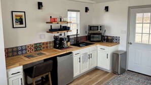 Eine kleine Küche mit weißen Schränken, einer Holz Arbeitsplatte, einer Kaffeemaschine, einem Toaster und einem Kühlschrank.