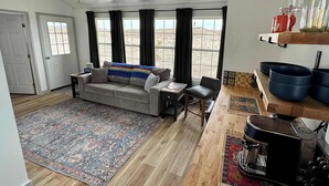 Ein Wohnzimmer mit einer Couch, einem Couchtisch, einem Teppich, einem Deckenventilator und Blick auf die Wüste durch große Fenster.