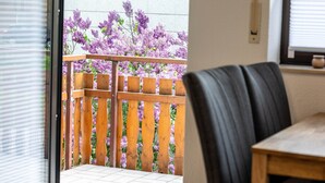 Un balcón con cerca de madera y flores moradas, una silla de cuero negro y una mesa de madera.