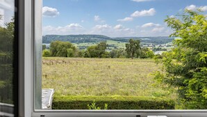 Blick durch ein Fenster auf eine ländliche Landschaft mit Feldern, Bäumen und fernen Hügeln.