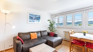 Ein modernes Wohnzimmer mit einer Ledersofa, einem Holztisch, einem Esstisch mit Stühlen, einer Stehlampe und einem großen Fenster mit Blick.