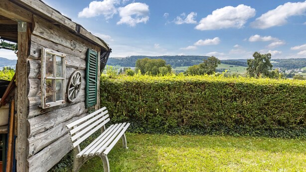 Ein rustikales Holzhaus mit einer Bank, einem Rundfenster und einer Hecke im Vordergrund.