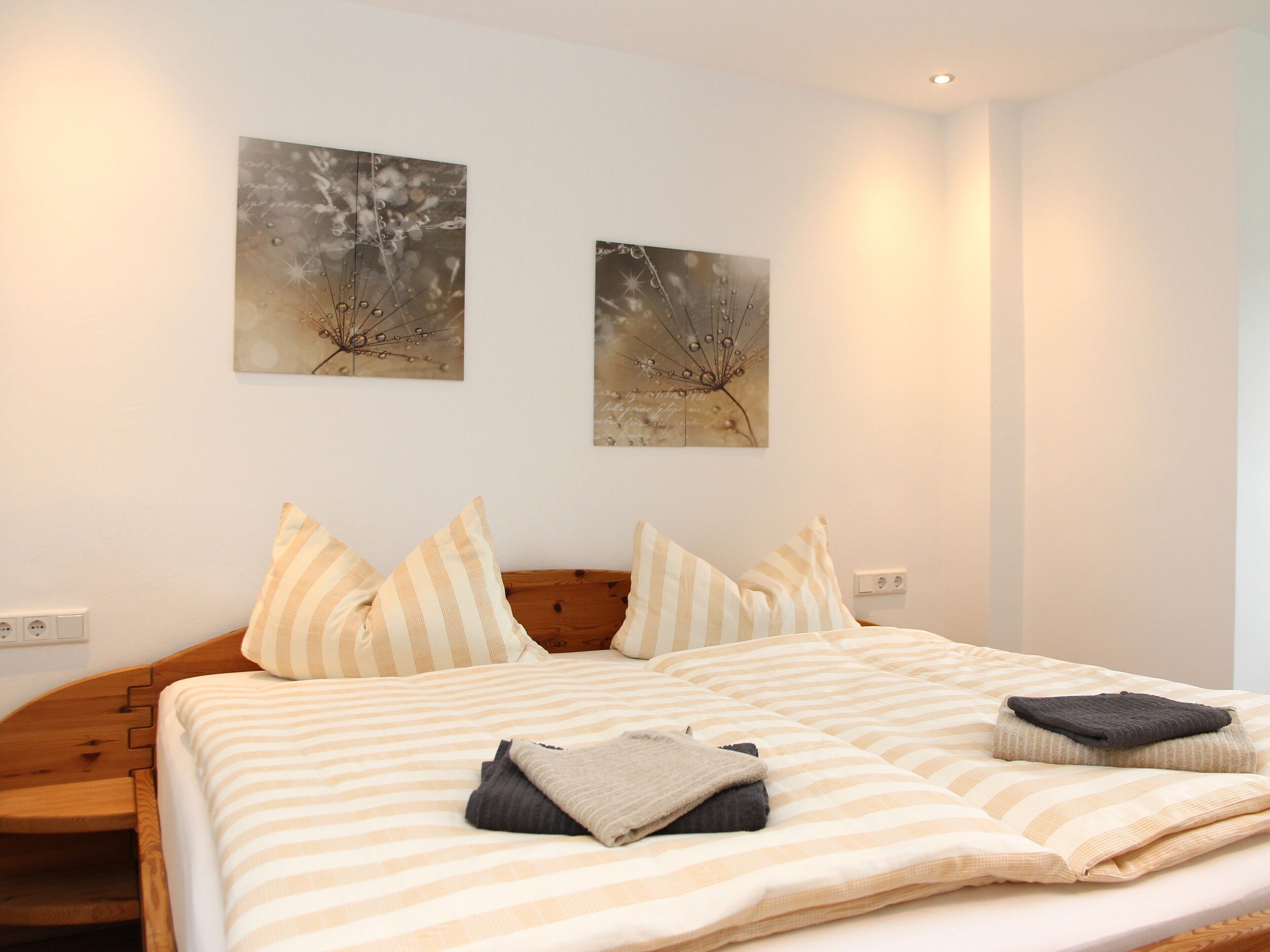 Una cama bien tendida con ropa de cama a rayas, un cabecero de madera y dos obras de arte colgadas en la pared.