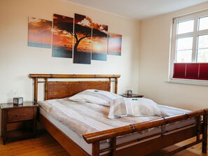 Una camera da letto con un letto in legno, un comodino, una panca da notte, una finestra con persiane e una parete decorata con tre quadri.