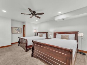 A bedroom with two wooden beds, a ceiling fan, recessed lighting, a nightstand with a lamp, and a wall-mounted picture.