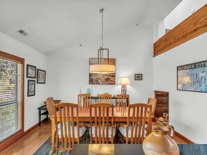 A dining area with a wooden table and chairs, a hanging light fixture, and framed artwork on the walls.