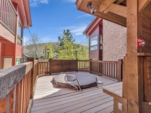 Une terrasse en bois avec un jacuzzi, une rambarde en bois et un bâtiment en pierre en arrière-plan.