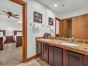 A hotel bathroom with a double sink vanity, wooden cabinets, a ceiling fan, and a large mirror.