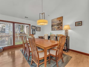 Un coin repas avec une table et des chaises en bois, un tableau accroché au mur et une vue à travers la porte vitrée.