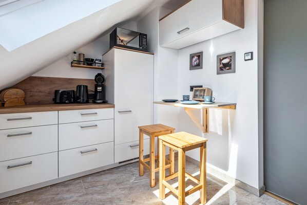 A compact kitchen with white cabinets, a wooden countertop, a microwave, a coffee maker, and a small wooden stool.