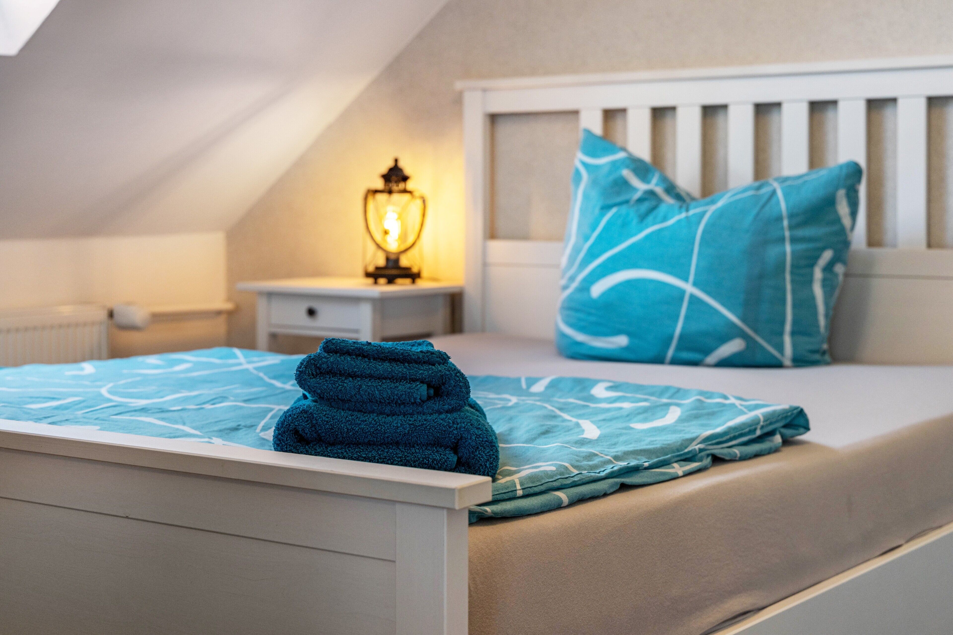 Un dormitorio con cama, mesita de noche, lámpara y ventana.