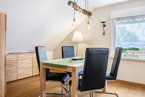A dining area with a wooden table, black chairs, a green tablecloth, and pendant lights.