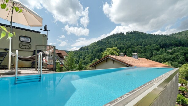 A swimming pool with a concrete edge, a sun umbrella, and a view of a forested hill. - Base Camp 'Poolhouse' with Private Pool and Black Forest Views (Bad Wildbad)