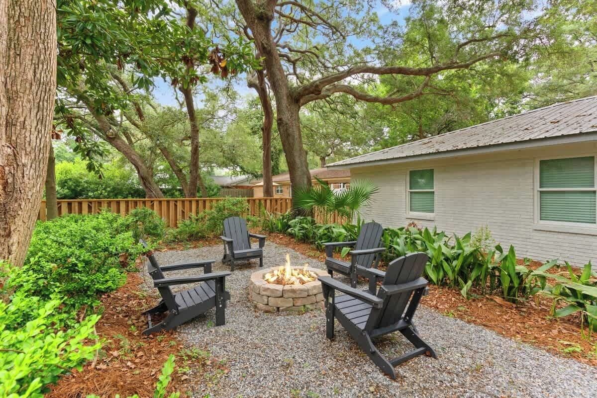 A patio with Adirondack chairs, a fire pit, and a house in the background.
