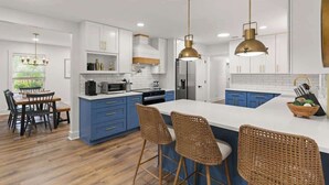 A modern kitchen with white cabinets, blue accents, and a central island with bar stools. - The Salty Tortoise - By Beach (Jekyll Island)