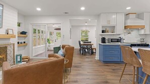 A modern kitchen with white cabinets, a blue countertop, and a dining area with a table and chairs. - The Salty Tortoise - By Beach (Jekyll Island)