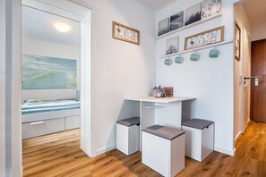 A compact room with a bed, a small table with stools, a shelf with decorative items, and a door leading to another room.