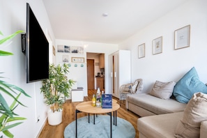 A modern living room with a flat-screen TV, a round coffee table, a sofa, and a dining area with a chair.