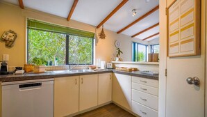 Una cocina con lavavajillas, un fregadero, una ventana con vista a árboles y una puerta con una agenda semanal.