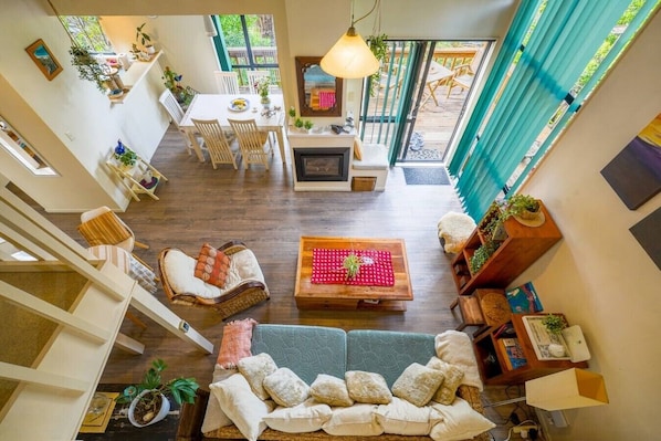 A spacious living area with a sofa, a coffee table, and a dining table. There is a fireplace, a staircase, and a view of the outdoors.
