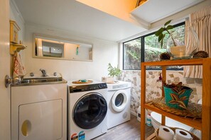 Une petite buanderie comprenant un lave-linge, un sèche-linge et une petite étagère où sont rangés les produits de toilette.