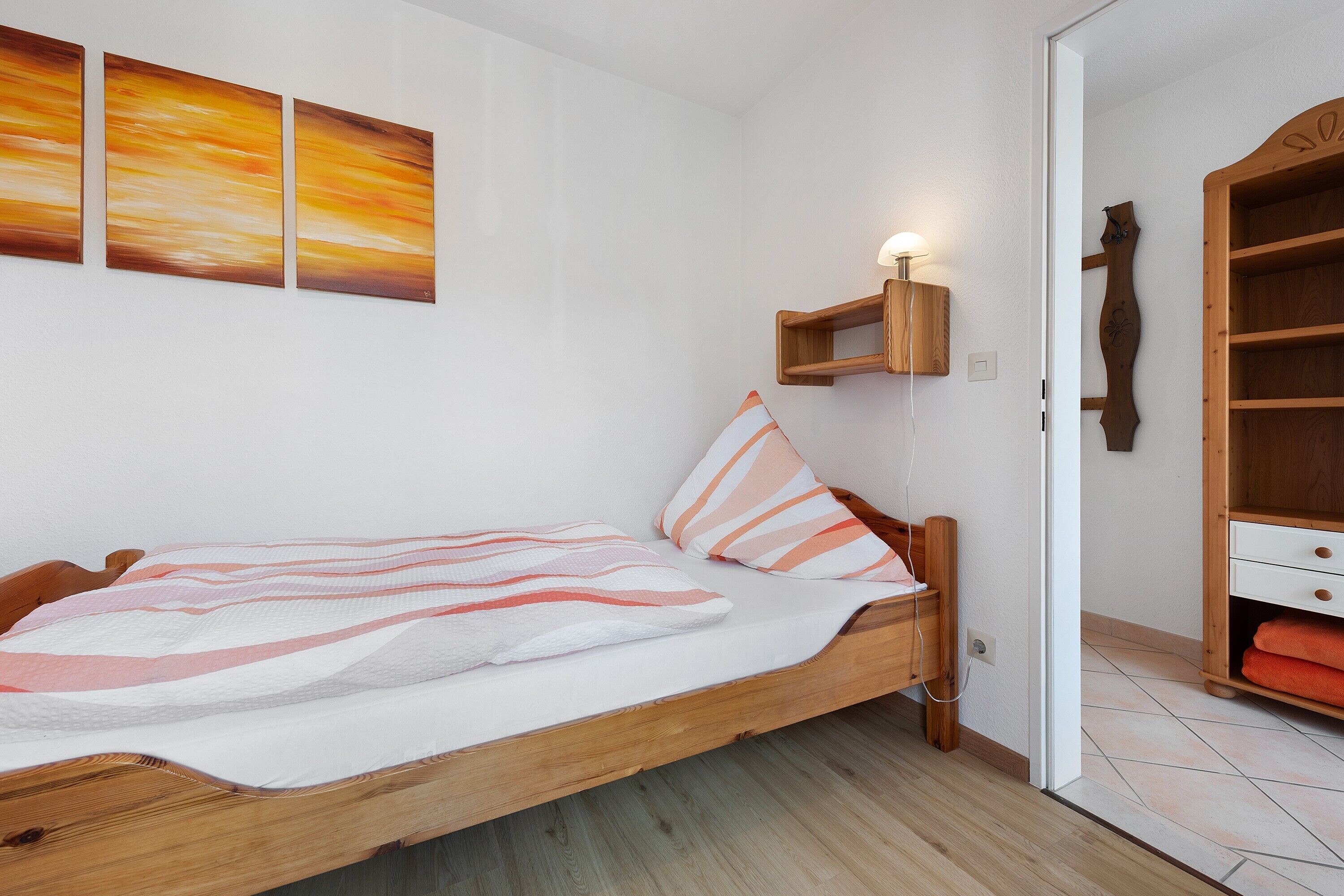 Un lit simple avec une couverture à rayures, une tête de lit en bois et une table de chevet avec une lampe.