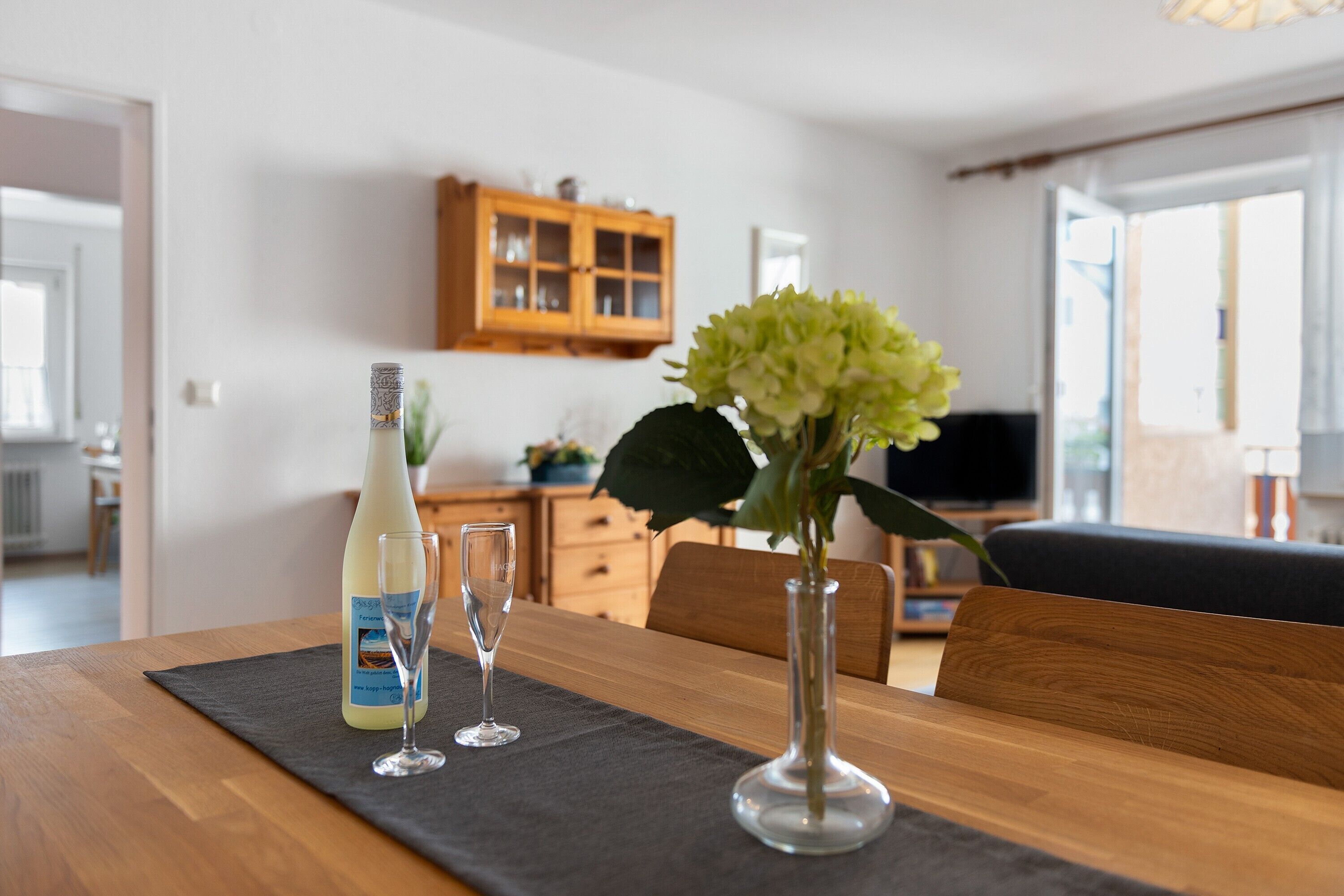 Ein Esstisch mit einer Flasche, zwei Gläsern und einer Blumenvase.