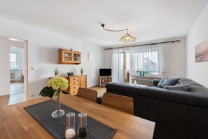Een moderne woonkamer met een bank, een eettafel met een vaas en zoutstrooiers, een houten kast en een televisie.