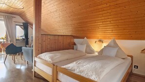 Ein Zimmer mit Holzboden, zwei Betten mit weißer Bettwäsche, ein Stuhl und ein kleiner Tisch.