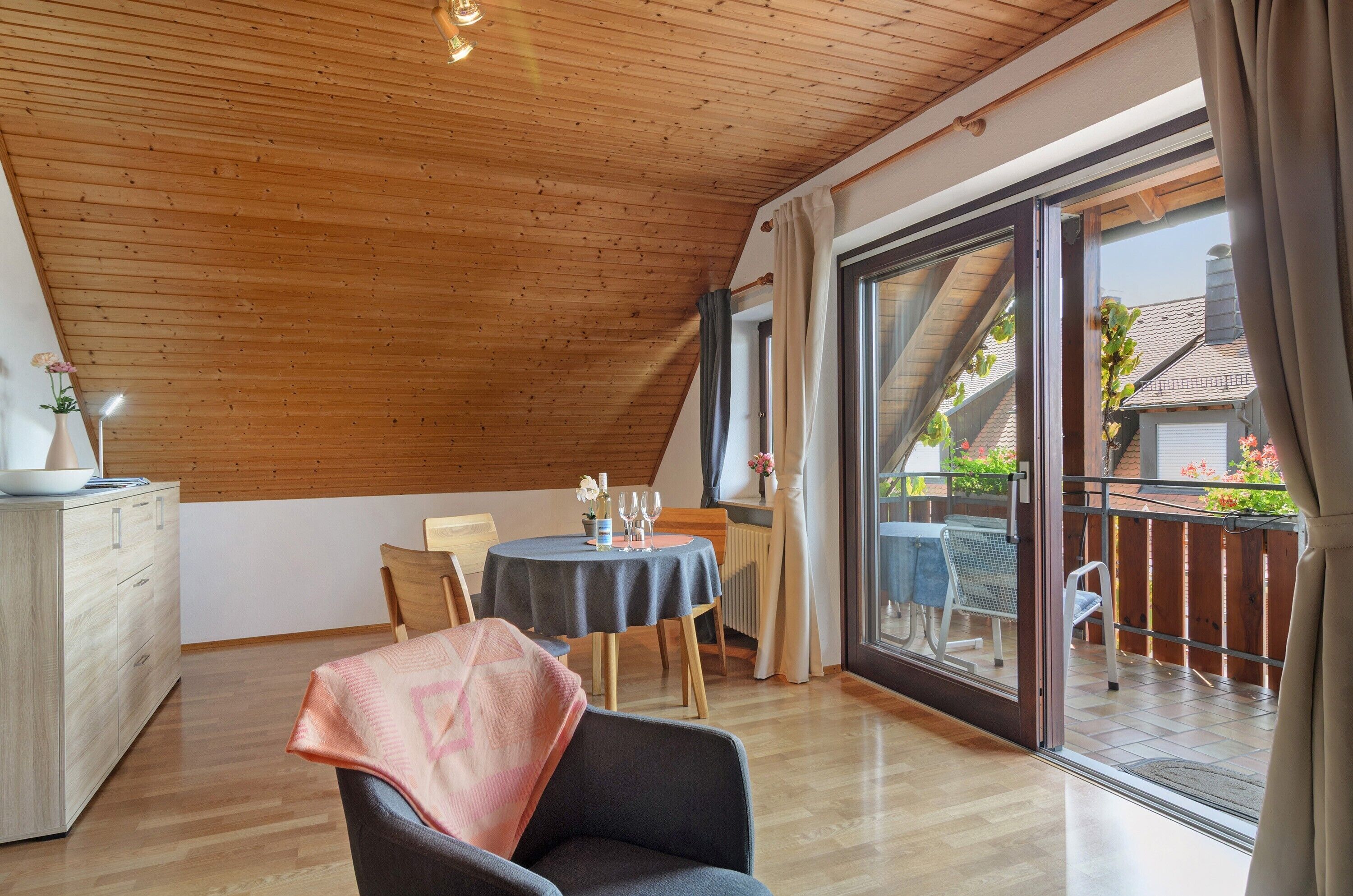 Ein Zimmer mit Holzboden, einem Esstisch mit Stühlen, einer Couch und einer Glastür, die zu einem Außenbereich führt.