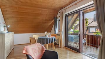 Ein Zimmer mit Holzboden, einem Esstisch mit Stühlen, einer Couch und einer Glastür, die zu einem Außenbereich führt.