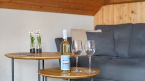 Ein Holztisch mit einer Flasche und zwei Gläsern, eine Vase mit Blumen, und ein graues Sofa in einem Raum mit Holzboden und -wänden.